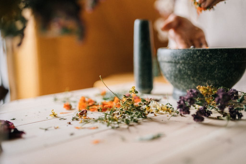 Close-up of dried flowers and herbs being processed in a mortar and pestle on a wooden table.